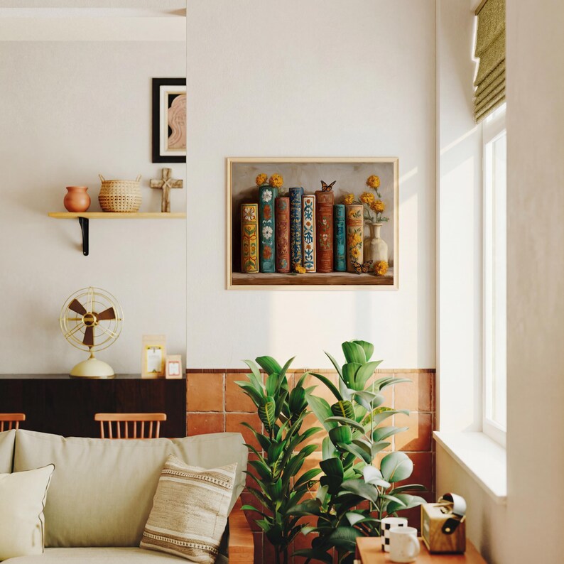 May include: A framed print featuring a still life of antique books with colorful spines, a butterfly, and yellow flowers in a vase. The artwork is displayed on a white wall, with a shelf and other decorative items visible.