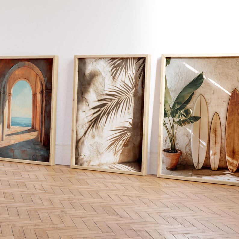 May include: Three framed art prints with a coastal theme. One print depicts an arched hallway overlooking the ocean. Another shows palm leaf shadows on a textured wall. The third features surfboards and a potted plant.
