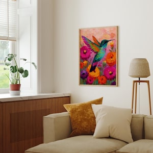 May include: A framed painting depicting a hummingbird in flight, with vivid colours. The bird features a turquoise body and multi-coloured wings, set against a backdrop of bright pink, orange, and purple flowers. The artwork is displayed in a living room.