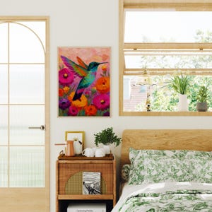 May include: A framed painting depicting a hummingbird with colourful wings and a long beak, amidst vibrant pink, orange, and purple flowers. The artwork has a textured, impressionistic style, with a light pink background.