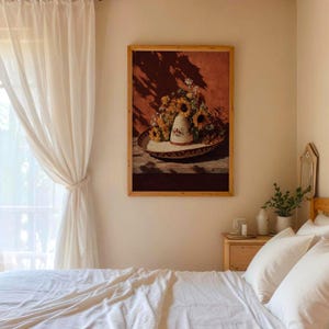 May include: A framed artwork depicts a still life with a sombrero, sunflowers, and other flowers. The sombrero is white with a patterned design. The background is a reddish-brown color, and the frame is made of wood.