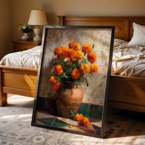 May include: A framed painting depicts a still life of orange marigold flowers in a brown terracotta vase. The flowers are vibrant against a textured, neutral background. The painting is leaning against a bed frame.