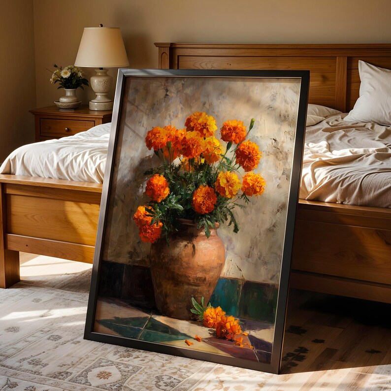 May include: A framed painting depicts a still life of orange marigold flowers in a brown terracotta vase. The flowers are vibrant against a textured, neutral background. The painting is leaning against a bed frame.