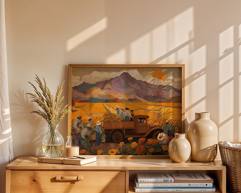May include: A framed painting depicts a harvest scene with a truck loaded with sunflowers, figures in hats, and a mountain backdrop. The artwork is displayed on a wooden dresser with vases, books, and a glass vase with wheat.