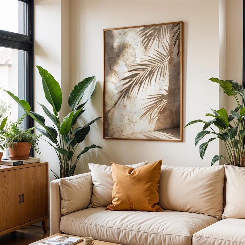 May include: A living room scene featuring a beige sectional sofa with several pillows, including a mustard-colored accent pillow. A framed artwork with palm leaf shadows hangs above the sofa. Potted plants add greenery to the space.