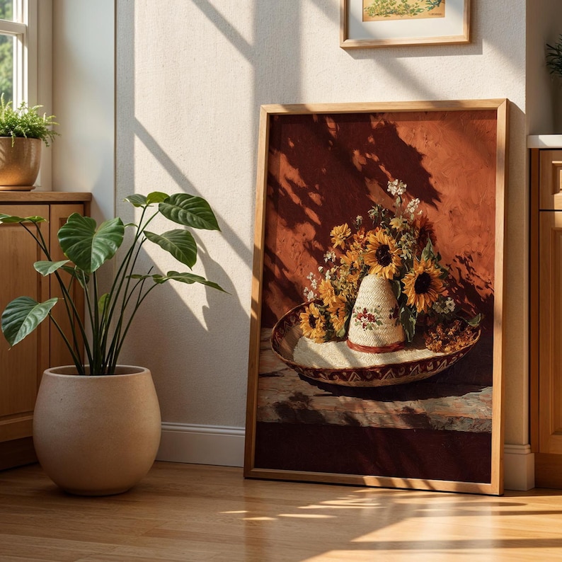 May include: A framed artwork featuring a still life of sunflowers and a straw hat with floral embroidery. The artwork is set against a reddish-brown background, with a wooden frame. The image is lit by natural light, creating shadows.