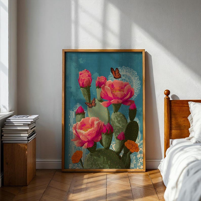 May include: A framed art print featuring a cactus with large pink flowers and orange accents against a teal background. Butterflies and decorative lace patterns are also present. The artwork is displayed in a room with a wooden floor.