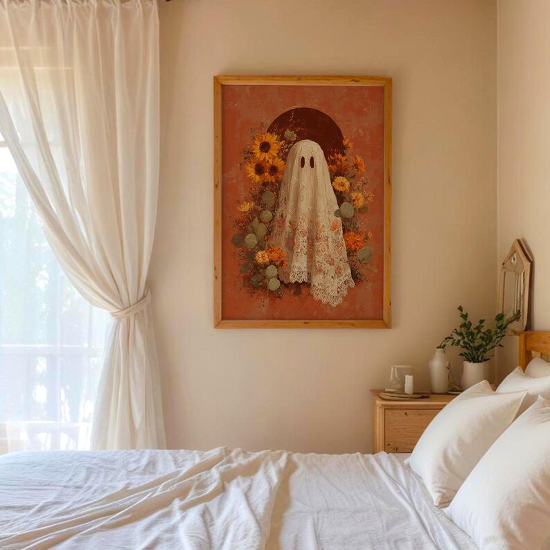 May include: A framed artwork featuring a ghost figure draped in a floral lace cloth, surrounded by sunflowers and other flowers. The artwork is set against a reddish-orange background with a dark brown semi-circle. The frame is made of light brown wood.