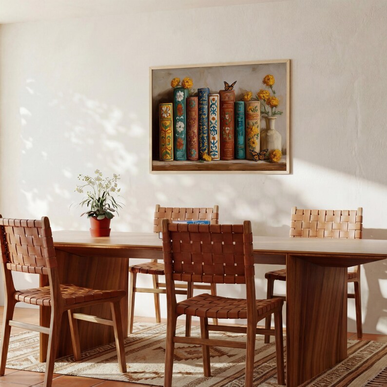 May include: A dining room scene featuring a wooden table and chairs with woven leather seats. A framed artwork above the table depicts a collection of colorful books and flowers. The room has a warm, inviting atmosphere.