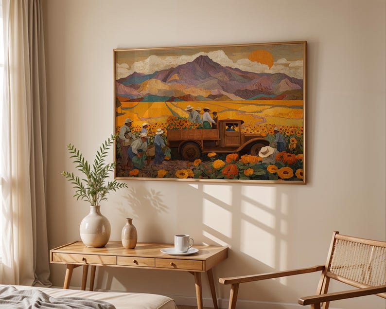 May include: A framed artwork depicts a harvest scene with a vintage truck loaded with sunflowers. The painting features a field of sunflowers, workers, and a mountain range under a setting sun. The artwork is displayed above a wooden table with a vase and a coffee cup.