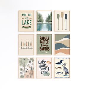 May include: Nine framed art prints with a lake theme. The prints feature illustrations of paddles, a lake scene, and text that reads "Meet Me at the Lake", "Paddle Faster, I hear Banjos", and "Lake Hair, Don't Care". The color palette includes greens, blues, and beige.