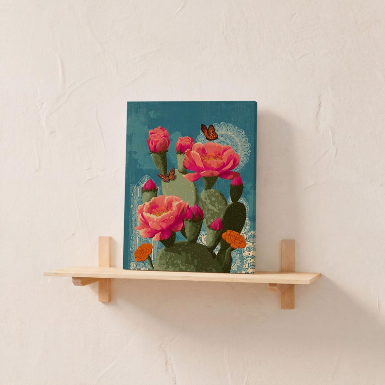 Pode incluir: Impress&atilde;o em tela com um cacto estilizado com grandes flores rosa e borboletas laranja sobre um fundo azul-petr&oacute;leo. A obra de arte &eacute; exibida em uma prateleira de madeira clara, criando um elemento decorativo de parede.