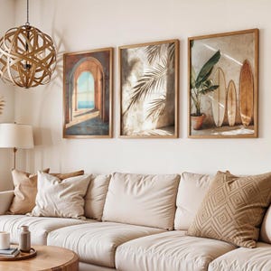 May include: Three framed wall art pieces with wooden frames. The art features an archway, palm leaves, and surfboards. The room also includes a beige sofa, throw pillows, and a wooden coffee table.