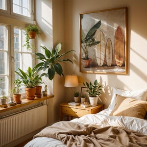 May include: A bedroom scene with a framed artwork of surfboards and a potted plant. The room features a bed with a tan blanket and pillow, a wooden nightstand with a lamp, and a window with potted plants. The overall color scheme is warm and inviting.