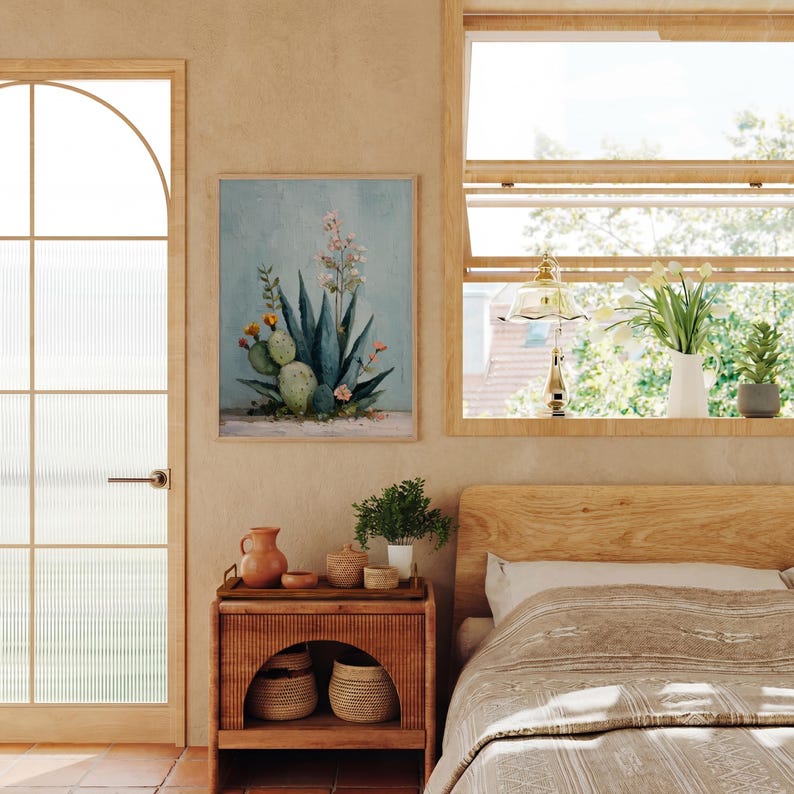 May include: A framed botanical print featuring a watercolor painting of a cactus and other desert plants. The artwork is displayed on a light blue background. The room also includes a wooden nightstand, a bed, and a window with plants.