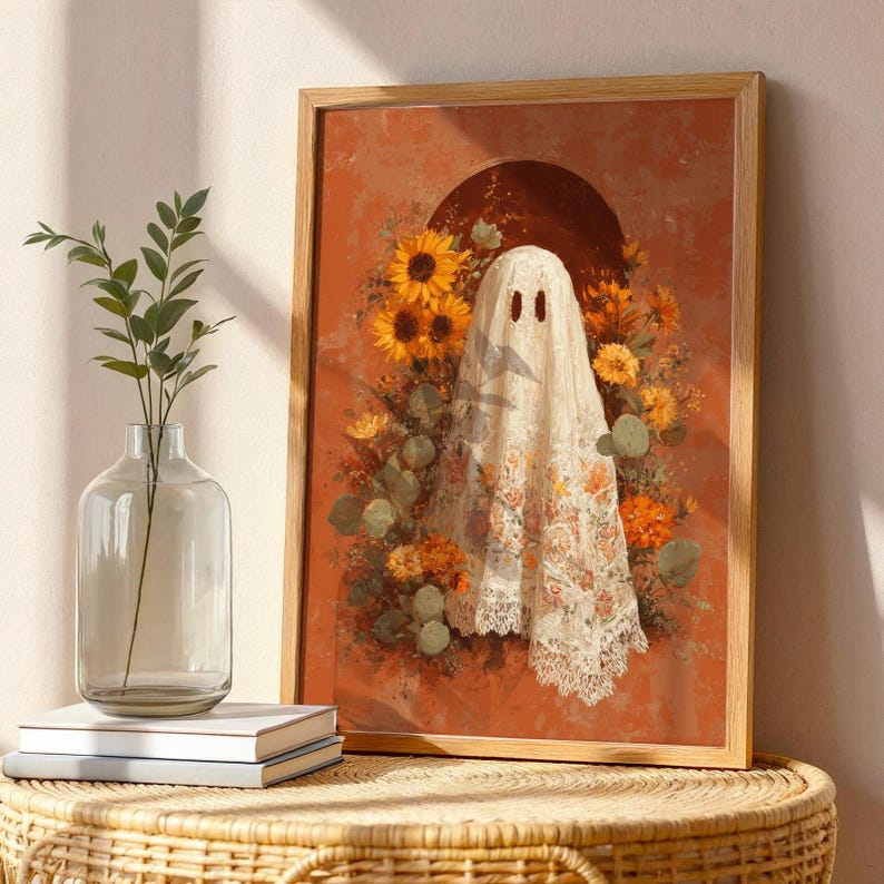 May include: A framed art print featuring a ghost figure draped in a floral patterned cloth, surrounded by sunflowers and other orange and yellow flowers. The artwork has a warm, autumnal color palette and is set against a terracotta background.