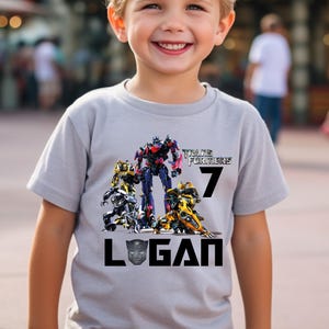 May include: A gray t-shirt with a Transformers graphic and the text "Transform Forever" and "7". The name "Logan" is printed below the graphic.