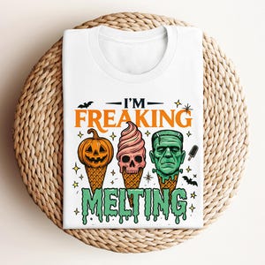 K&ouml;nnte beinhalten: Wei&szlig;es T-Shirt mit einem Halloween-Motiv. Das Design zeigt einen K&uuml;rbis, ein eiscreme in Sch&auml;delform und Frankensteins Monster, die alle schmelzen. Der Text lautet "I'M FREAKING MELTING".