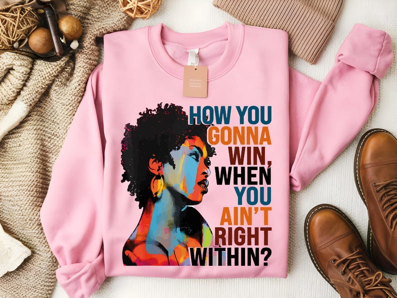 May include: Pink sweatshirt with a colorful illustration of a woman with an afro and the text "How you gonna win, when you ain't right within?"