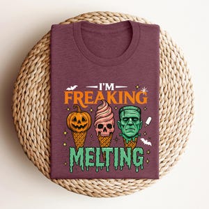 K&ouml;nnte beinhalten: Burgunderfarbenes T-Shirt mit einem Halloween-Motiv. Das Design zeigt drei Eist&uuml;ten mit gruseligen Gesichtern: einen K&uuml;rbis, einen Totenkopf und Frankensteins Monster. Der Text lautet "I'M FREAKING MELTING".