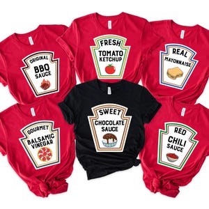 May include: Six red and black t-shirts with a white ketchup bottle design. Each shirt features a different type of sauce: BBQ, Tomato Ketchup, Mayonnaise, Balsamic Vinegar, Chocolate Sauce, and Red Chili Sauce.