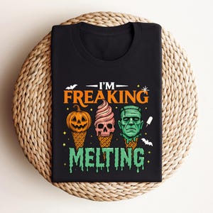 K&ouml;nnte beinhalten: Schwarzes T-Shirt mit einem Halloween-Motiv. Das Design zeigt drei Eiswaffeln mit gruseligen Gesichtern: einen K&uuml;rbis, einen Totenkopf und Frankensteins Monster. Der Text lautet "I'm Freaking Melting."