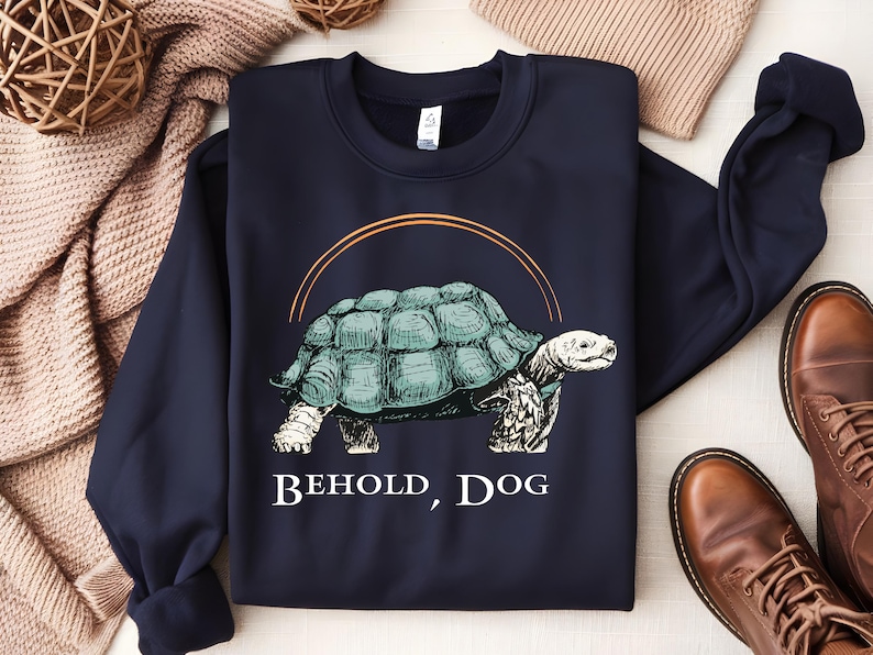 May include: A navy blue sweatshirt with a graphic of a turtle walking with the text "Behold, Dog" printed below it.