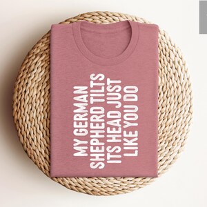 May include: A pink t-shirt with the text "My German Shepherd Tilts Its Head Just Like You Do" printed in white.