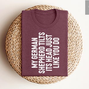 May include: A maroon t-shirt with the text "My German Shepherd Tilts Its Head Just Like You Do" printed in white.