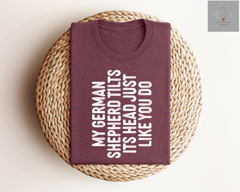 May include: A maroon t-shirt with the text "My German Shepherd Tilts Its Head Just Like You Do" printed in white.
