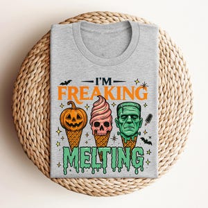 K&ouml;nnte beinhalten: Ein graues T-Shirt mit einem Halloween-Motiv. Das Design zeigt einen K&uuml;rbis, einen Totenkopf und Frankensteins Monster als Eist&uuml;ten, mit dem Text "I'M FREAKING MELTING".