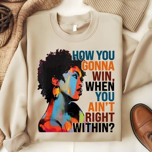 May include: Beige sweatshirt with a colorful illustration of a woman with an afro and the text "HOW YOU GONNA WIN, WHEN YOU AIN'T RIGHT WITHIN?"
