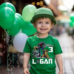May include: Green t-shirt with a Transformers graphic and the number 3. The shirt also has the name Logan printed on it.