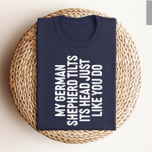 May include: A navy blue t-shirt with white text that reads "My German Shepherd Tilts Its Head Just Like You Do."