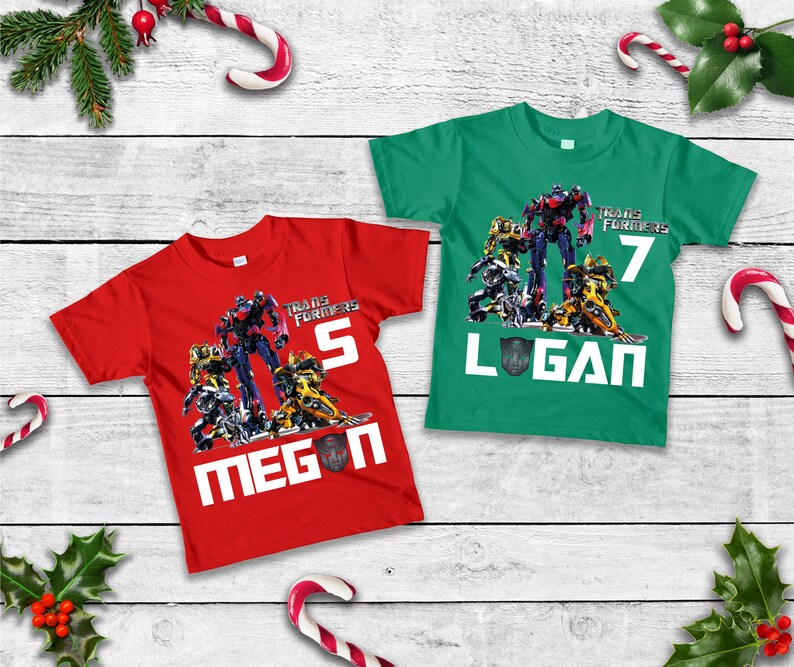 May include: Two red and green t-shirts with a Transformers graphic and the names Megan and Logan. The shirts have the numbers 5 and 7 on them.