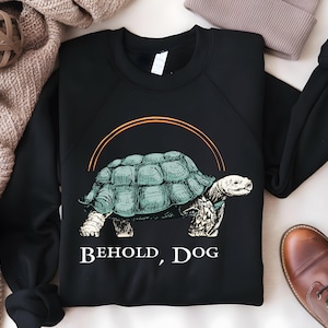 May include: Black sweatshirt with a graphic of a turtle with the text "Behold, Dog" printed on the front.