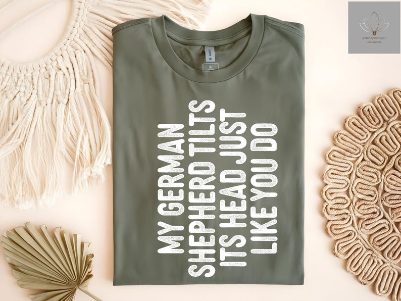 May include: A green t-shirt with white text that reads "My German Shepherd Tilts Its Head Just Like You Do."