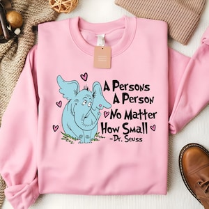 May include: Pink sweatshirt with a blue elephant illustration and the quote "A person's a person, no matter how small - Dr. Seuss".