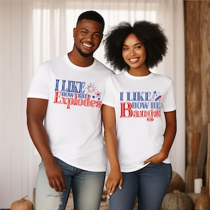 May include: Two people wearing white t-shirts with patriotic text. The shirt on the left says "I LIKE HOW SHE Explodes" in red and blue. The shirt on the right says "I LIKE HOW HE Bangs" in red and blue.
