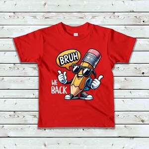 May include: Red t-shirt featuring a cartoon pencil wearing sunglasses and giving a thumbs up. The pencil is saying "BRUH" in a speech bubble, with the words "WE BACK" below. The design is centered on the shirt.