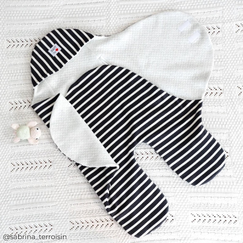 May include: A black and white striped swaddle with a white cotton lining. The swaddle is folded in half and has a small white tag with the word "Love" on it.