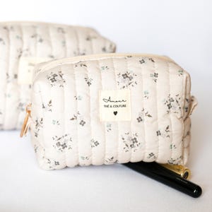 May include: A beige quilted makeup bag with a floral print and a white label that says "Amour The & Couture" with a small heart.