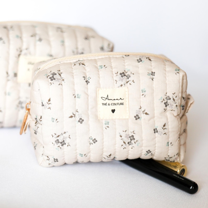 May include: A beige quilted makeup bag with a floral print and a white label that says "Amour The & Couture" with a small heart.
