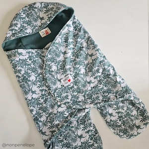 May include: A white hooded swaddle with a green jungle print featuring monkeys and leaves. The swaddle has a small red heart label with the text "HAUT  Kids" on it.