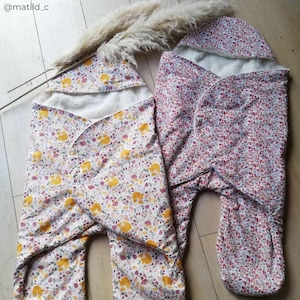 May include: Two baby swaddles with floral patterns. One swaddle is white with yellow foxes and the other is pink with red flowers. Both swaddles have a white hood.