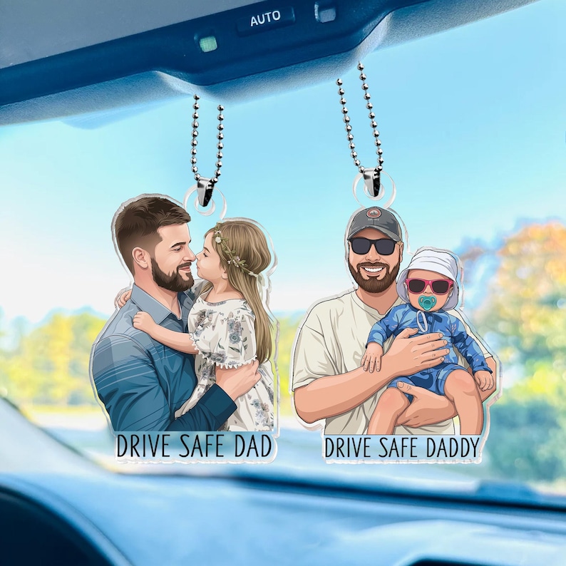 May include: Two car hanging ornaments with illustrations of fathers and children. One shows a father holding a child with the text "DRIVE SAFE DAD". The other shows a father holding a baby with the text "DRIVE SAFE DADDY".