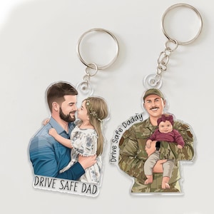 May include: Two clear acrylic keychains with silver keyrings. One keychain features a cartoon illustration of a man and a girl, with the text "DRIVE SAFE DAD". The other keychain shows a man in uniform holding a baby, with the text "Drive Safe Daddy".