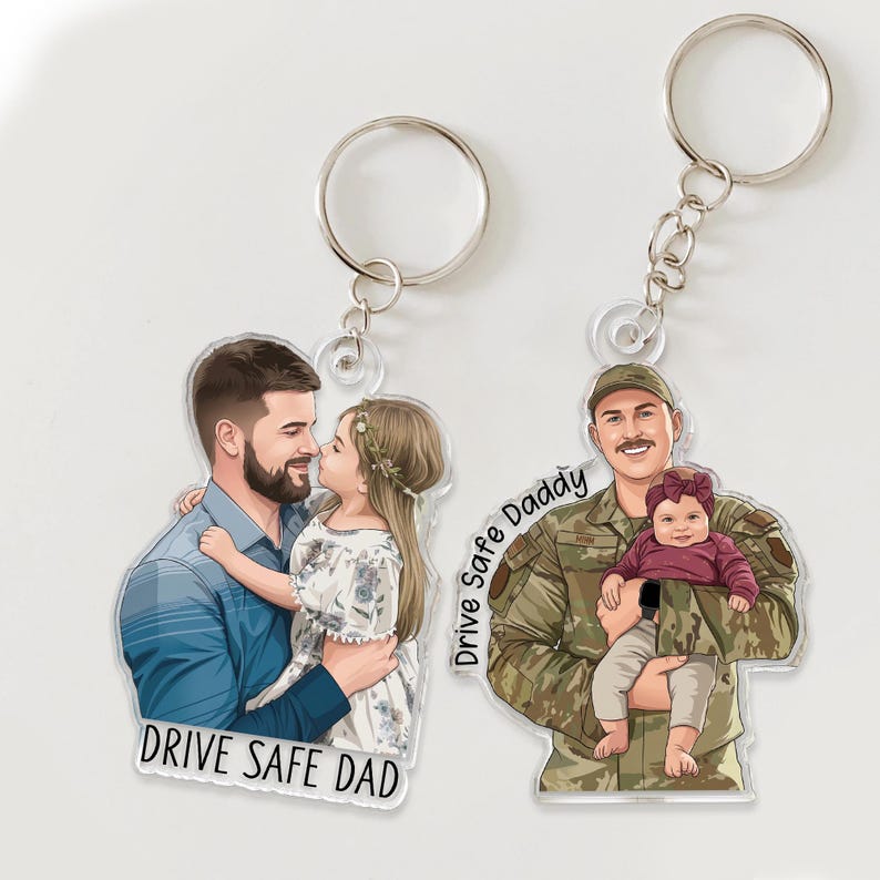 May include: Two clear acrylic keychains with silver keyrings. One keychain features a cartoon illustration of a man and a girl, with the text "DRIVE SAFE DAD". The other keychain shows a man in uniform holding a baby, with the text "Drive Safe Daddy".