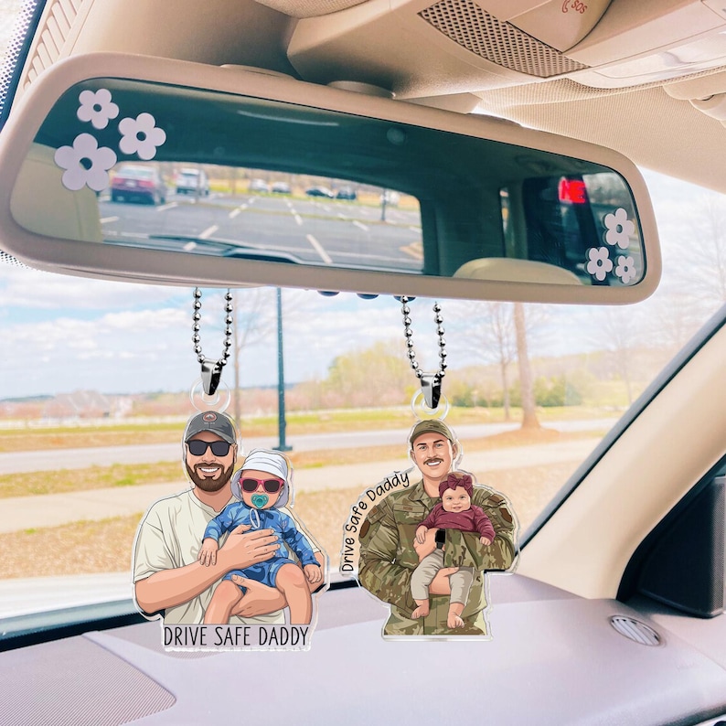 May include: Two car air fresheners with cartoon illustrations of a father and child. One shows a man in a baseball cap holding a baby, the other shows a man in a military uniform holding a baby. The text "Drive Safe Daddy" is on both.
