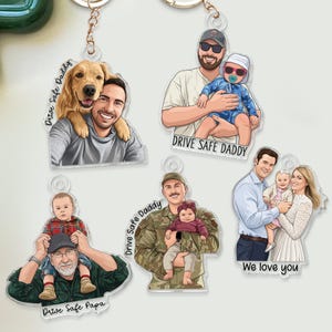 May include: Acrylic keychains featuring cartoon illustrations of people with pets and children. Each keychain has a different design, including a man with a dog, a father with a baby, and a family. Text includes "Drive Safe Daddy" and "We love you".